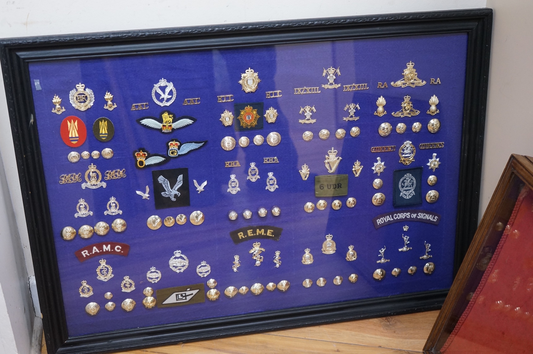 Two display cases containing military cap badges, buttons and shoulder titles, including; the Royal Medical Corps, the Royal Tank Regiment, the Royal Corps of Signals, the Royal Electrical and Mechanical Engineers, etc.